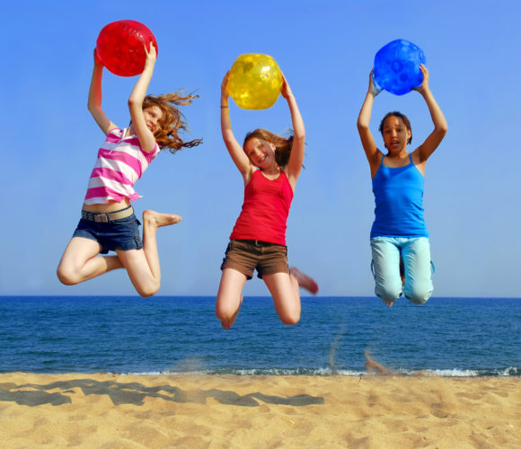 Three girls with colorful beach balls jumping on a seashore